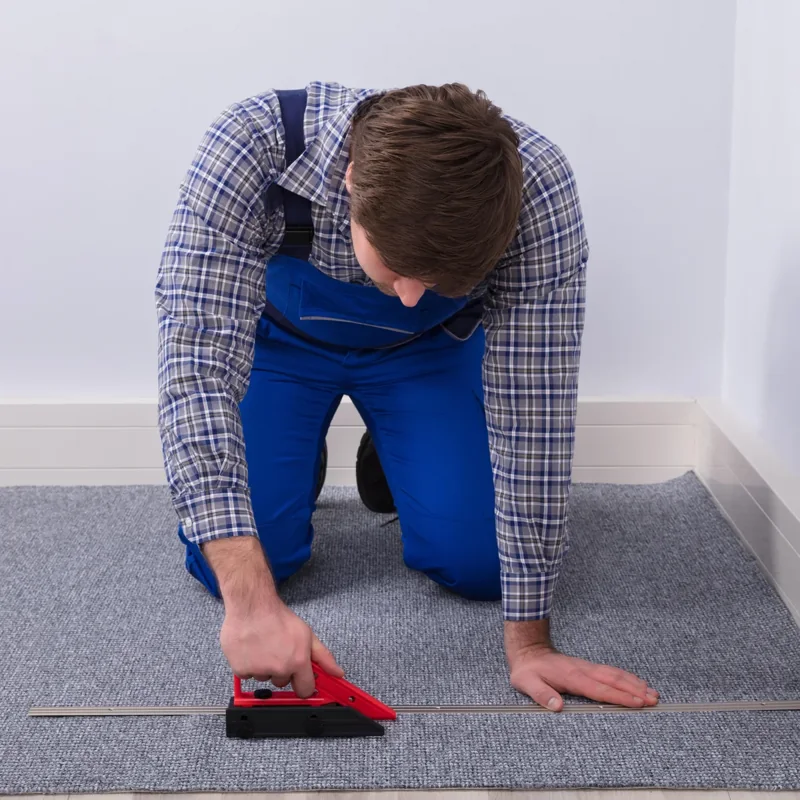 Installer using a carpet wall trimmer along a metal straightedge